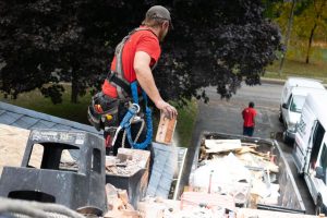 Construction worker removing brick debris from a roof into a hauling truck during a construction debris removal job in Fontana, CA
